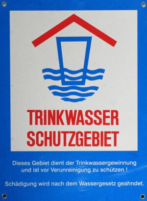 Schild - Trinkwasserschutzgebiet - blauer Hintergrund, rote Schrift - symbolisch: überdachte Tasse steht halb im Wasser